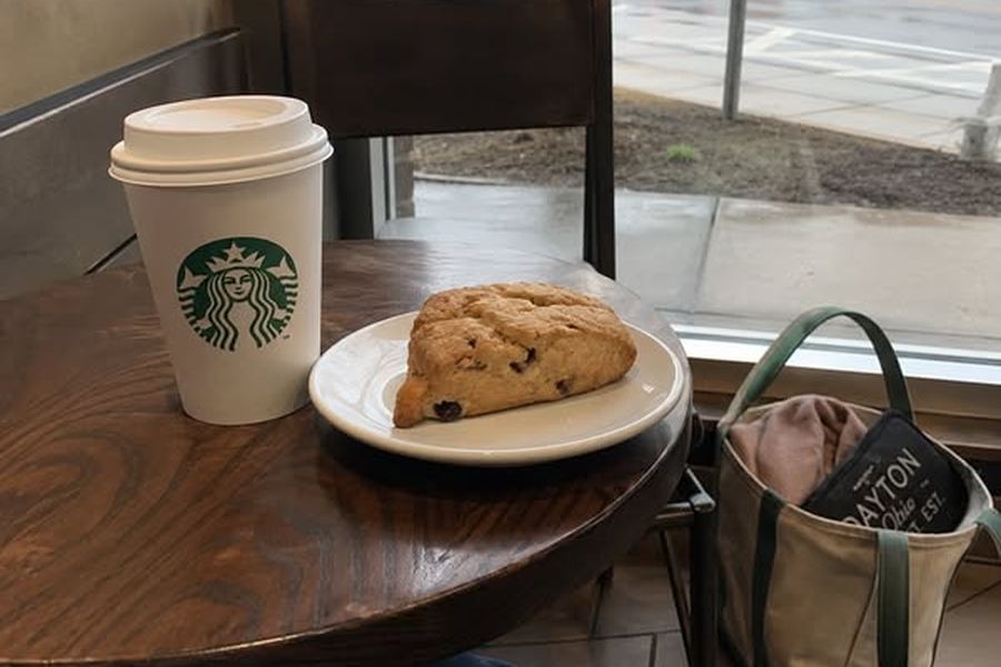 A coffee cup and a scone on a table by a window